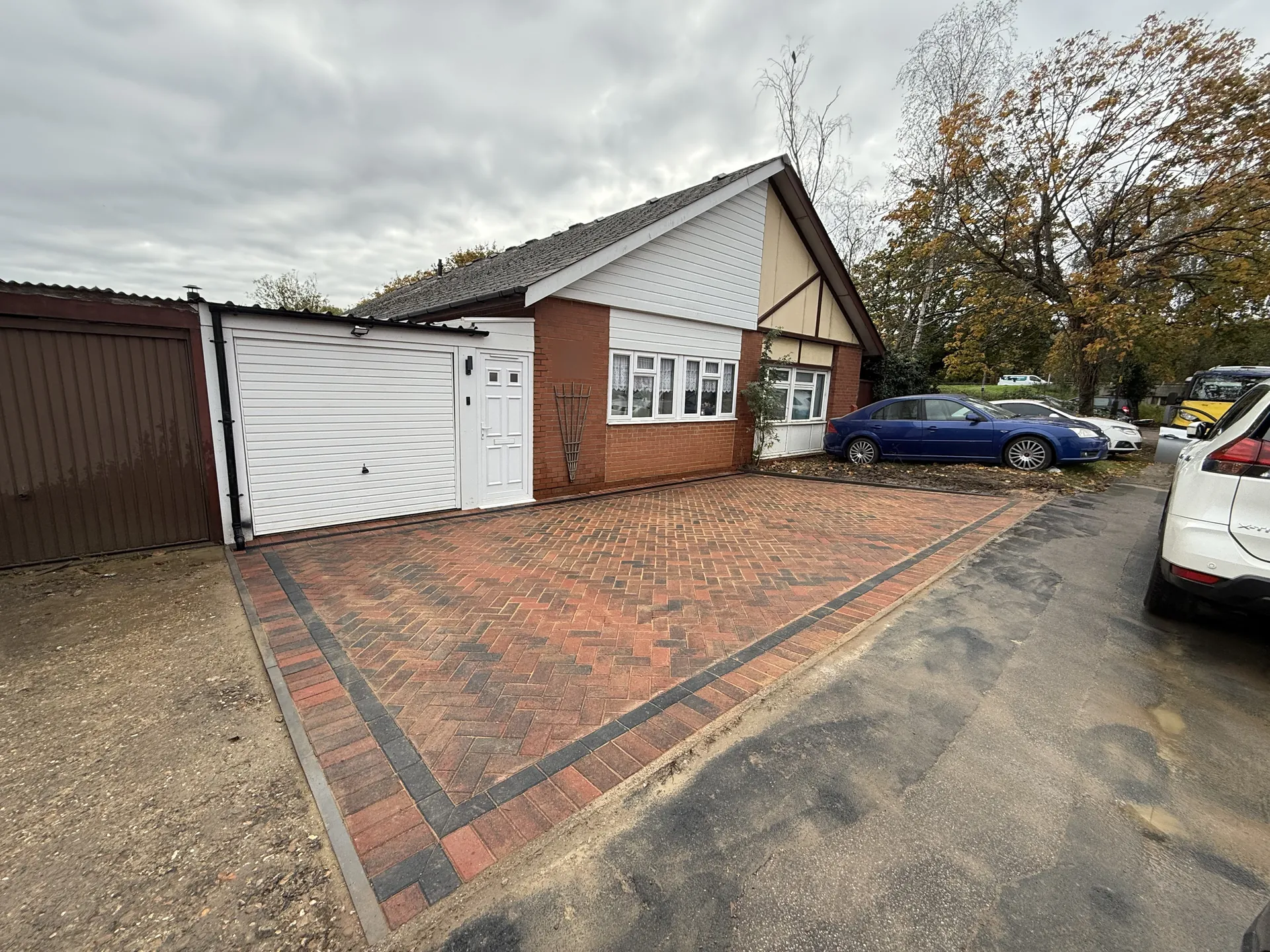 The finished driveway from the same corner, herringbone block paving with a charcoal border from the road up to the garage and house.