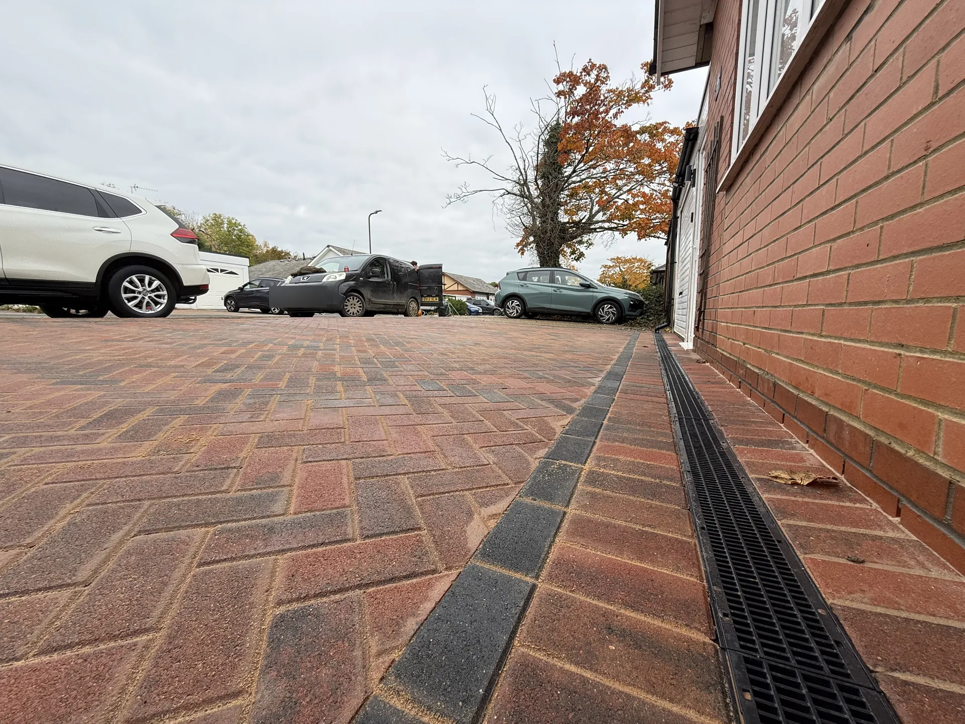 Ground-level view along the finished drive, herringbone on the left, the charcoal row and the drainage channel beside the house wall.