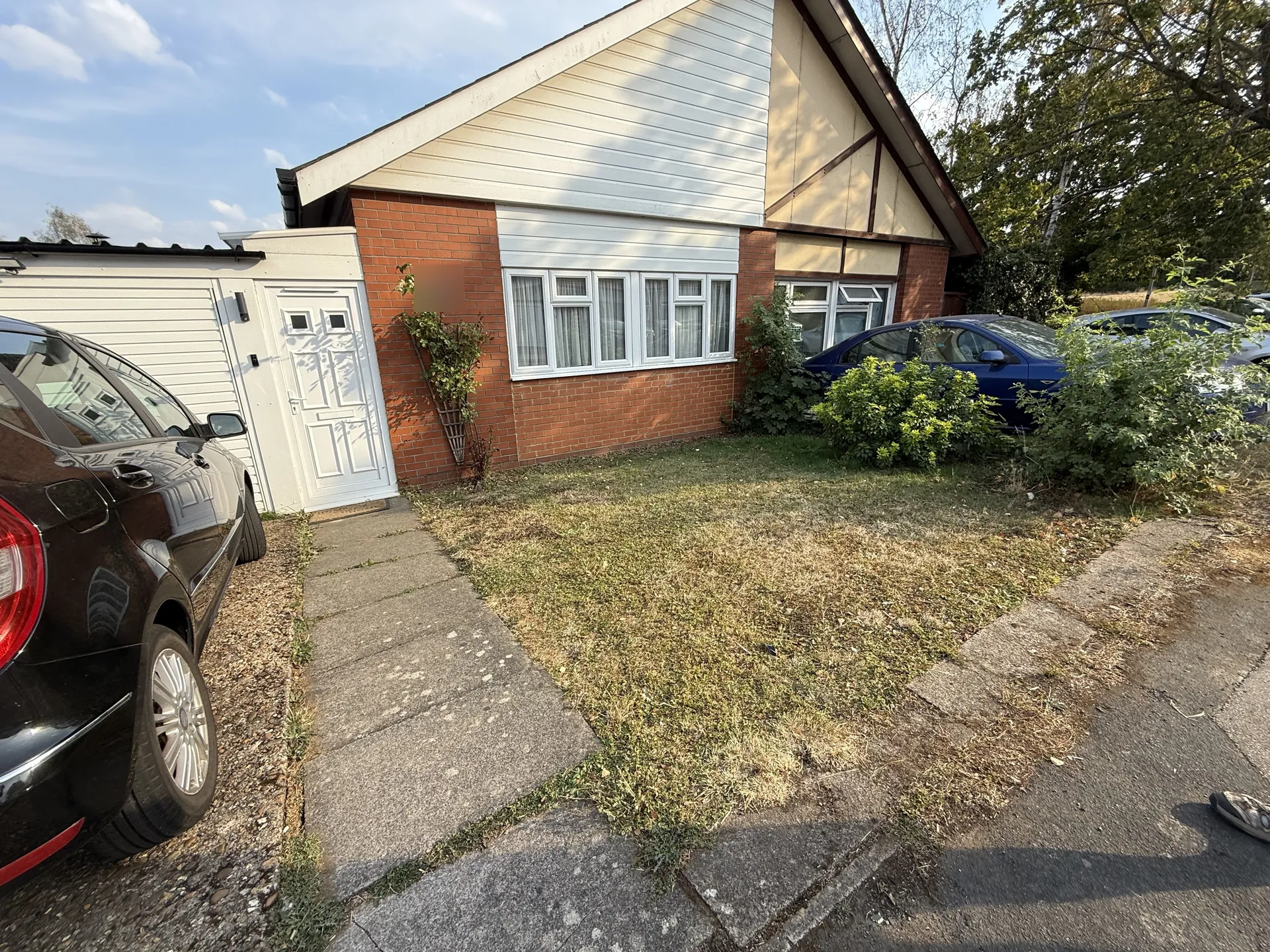 The front of the bungalow before work started, dry grass and an old slab path, with cars parked on gravel alongside.