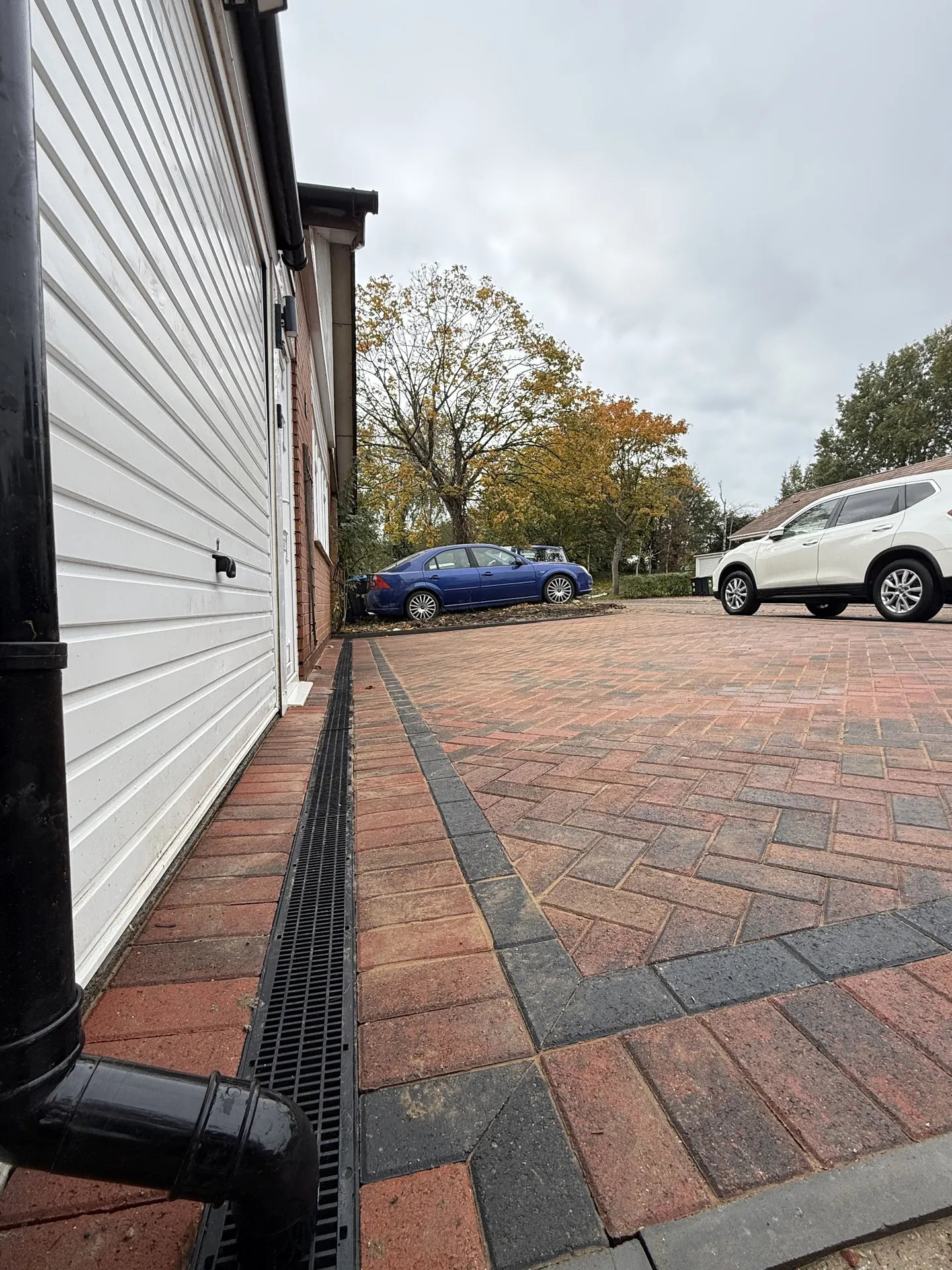 The drainage channel along the house wall, with the black garage downpipe running down beside it.