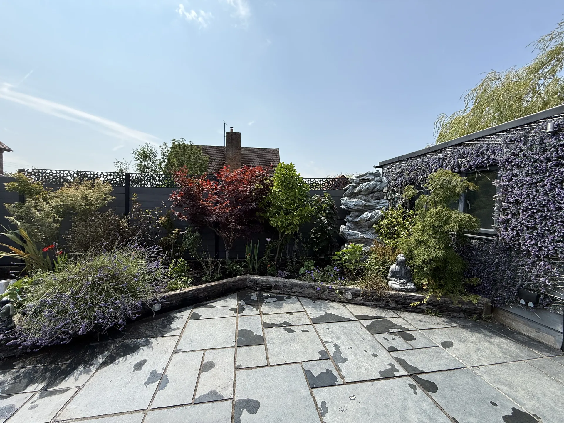 The corner by the summer house in July, planted with shrubs, grasses and a red-leaved tree behind the paving.