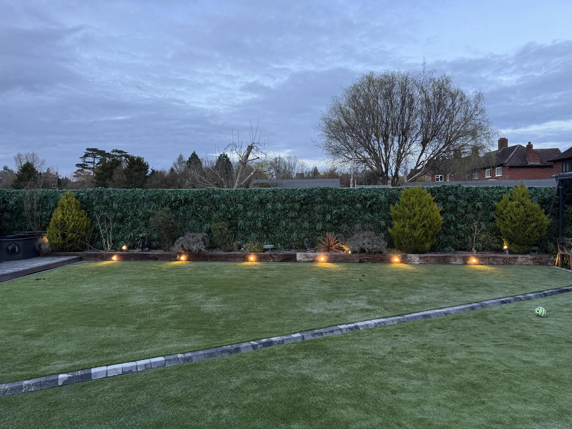 The relaid lawn at dusk, with lights along the border and the new charcoal block line between the two levels.