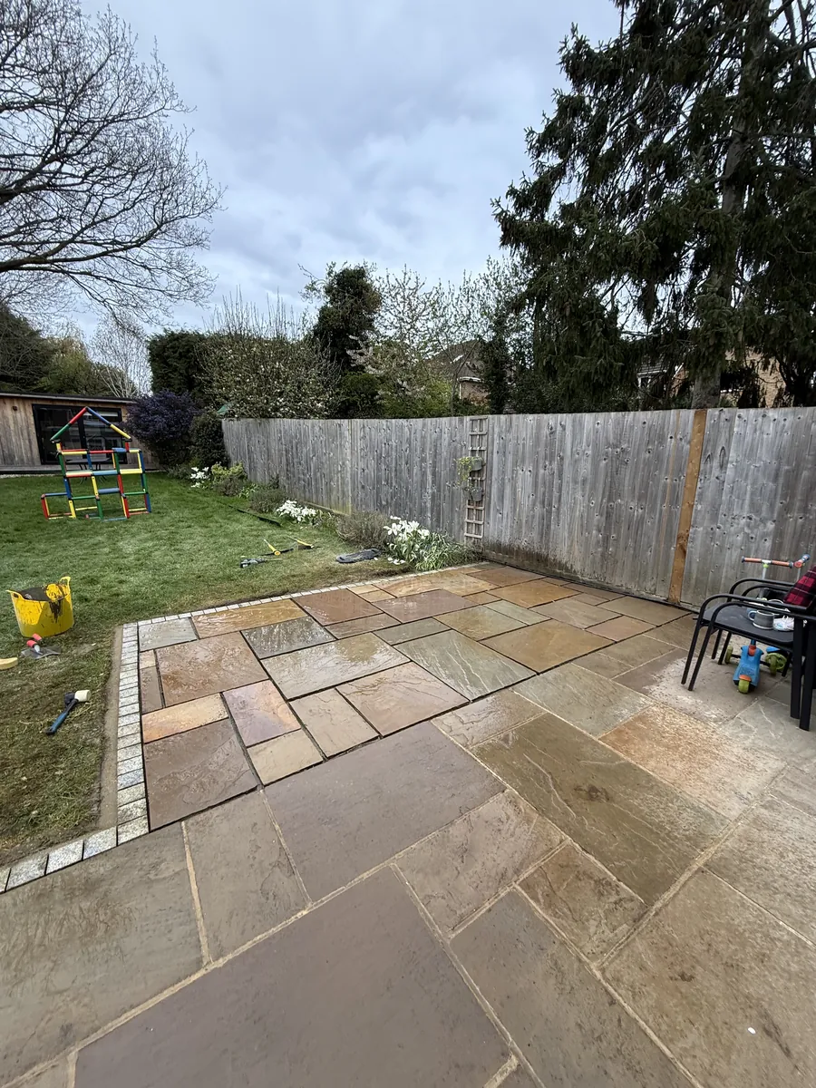 The same corner in April, with the outer section relaid, fresh dark pointing in the joints and a straight granite sett edge along the lawn.
