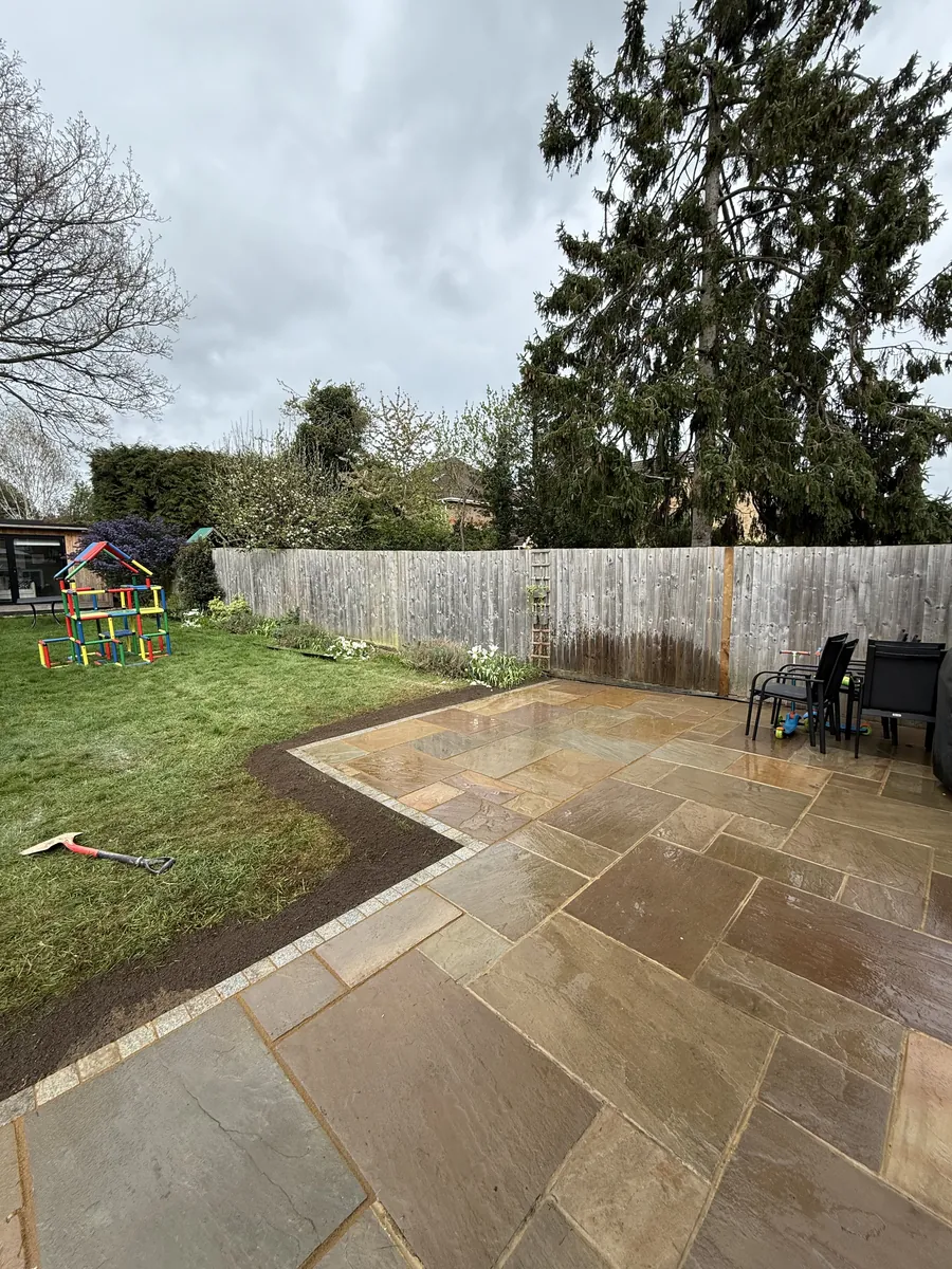 The relaid corner of the patio with its granite sett edge, and a strip of fresh soil between the edge and the lawn.