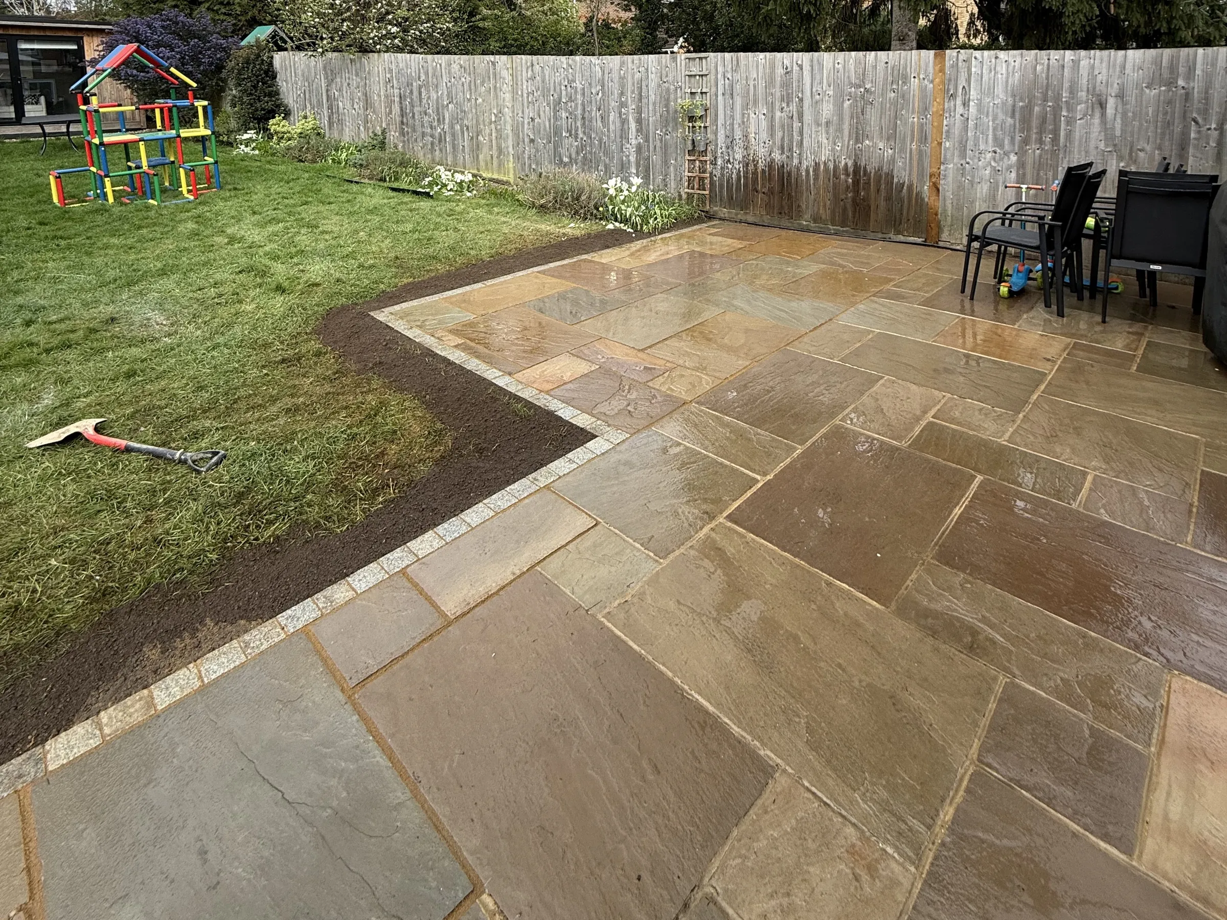 Finished stone patio in a Harpenden garden, with a straight granite sett edge and fresh soil along the lawn.