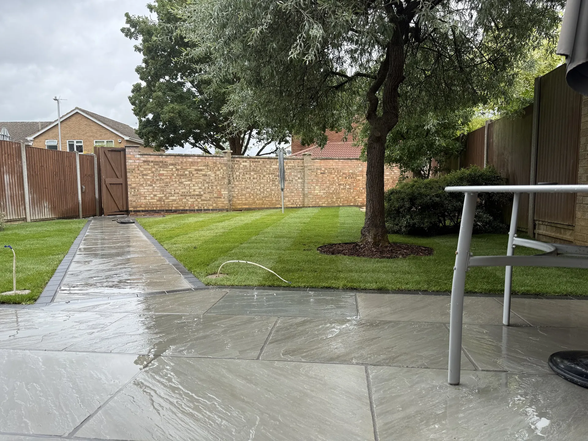 The new grey sandstone patio and a solid sandstone path running straight down the striped lawn to the back gate.