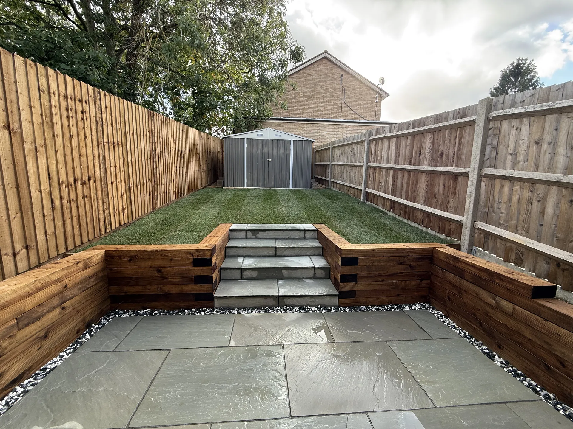 The finished garden from the back door: the sandstone patio, sleeper walls on three sides and the steps up to the lawn.