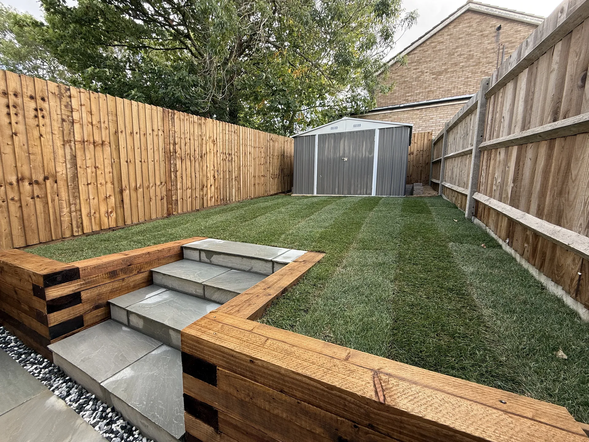The sandstone steps between the sleeper walls, leading up to the striped new lawn, with new fencing either side and the shed at the top.