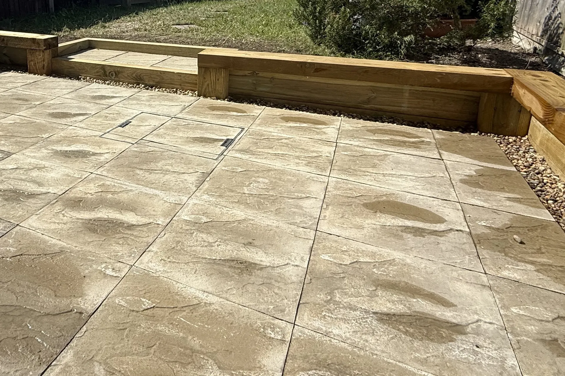 Close-up of the paved step set into the new green sleepers, a recessed access cover paved to match, and a strip of shingle along the edge.