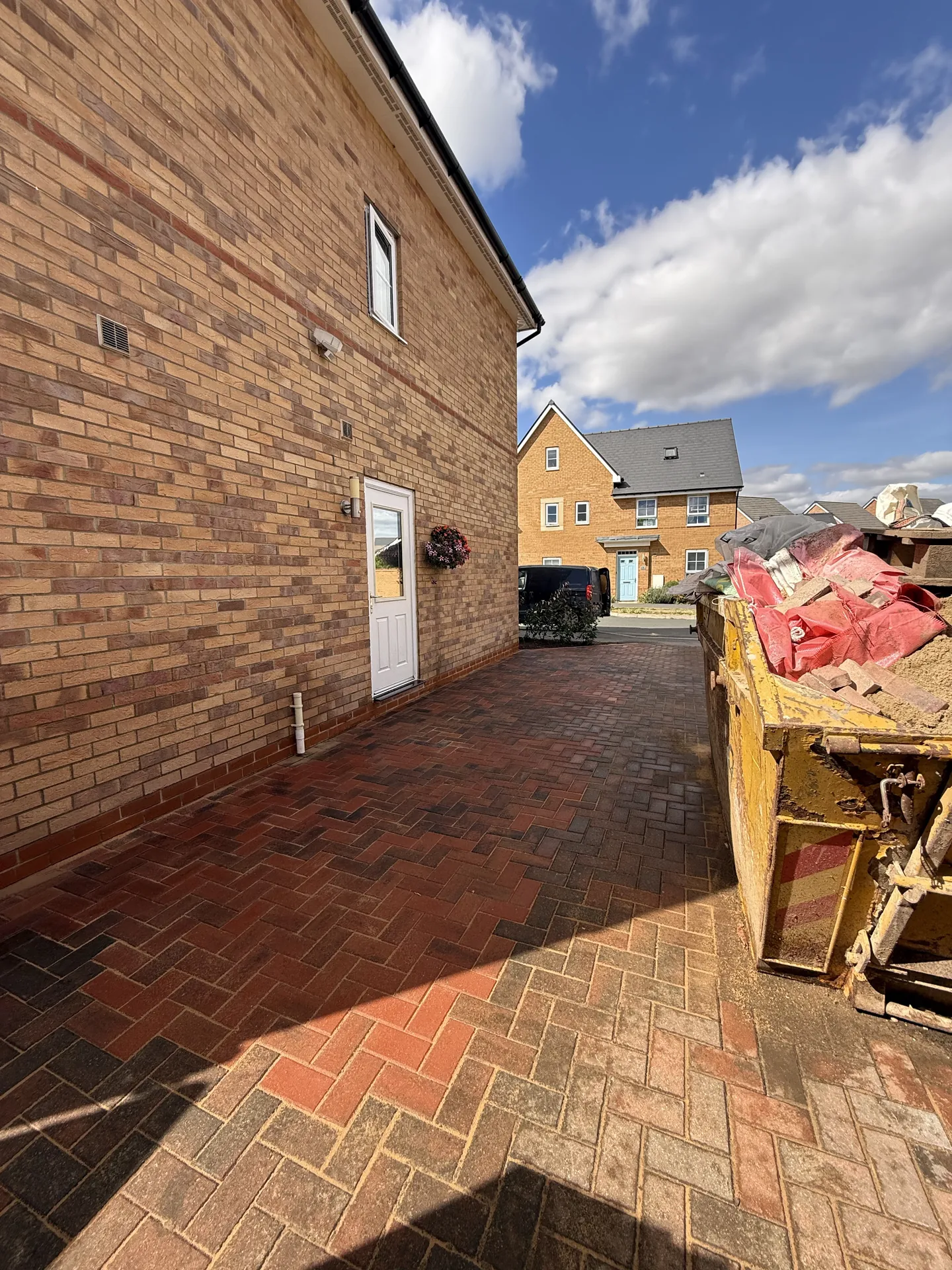 Looking along the side of the house, with new brindle blocks laid in herringbone right up to the wall and the paler blocks of the original drive in the foreground.