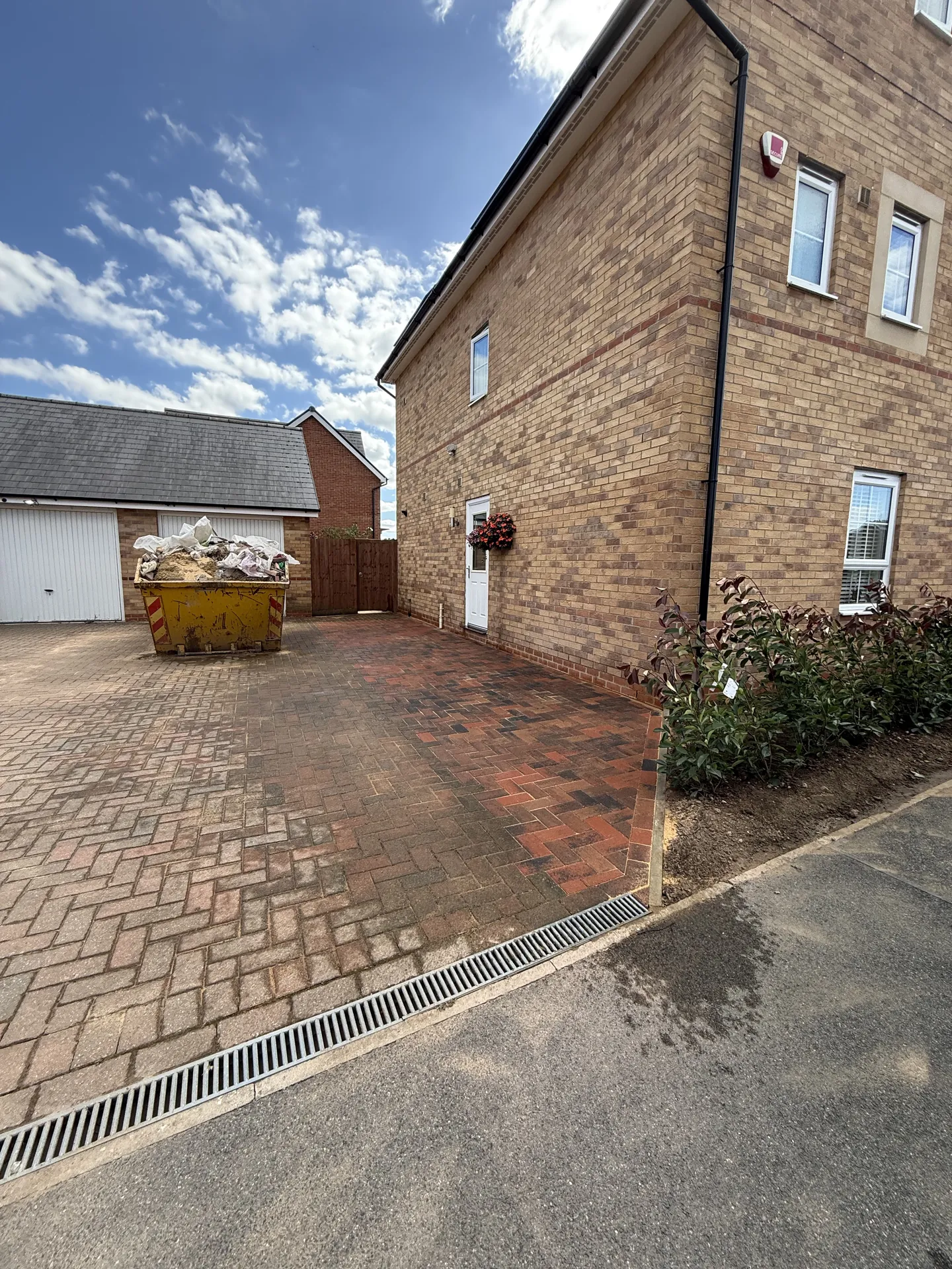 The finished drive from the pavement, with the new brindle block extension running up to the side of the house beside the existing drive, a skip still on the old paving, and a new red robin hedge along the front.