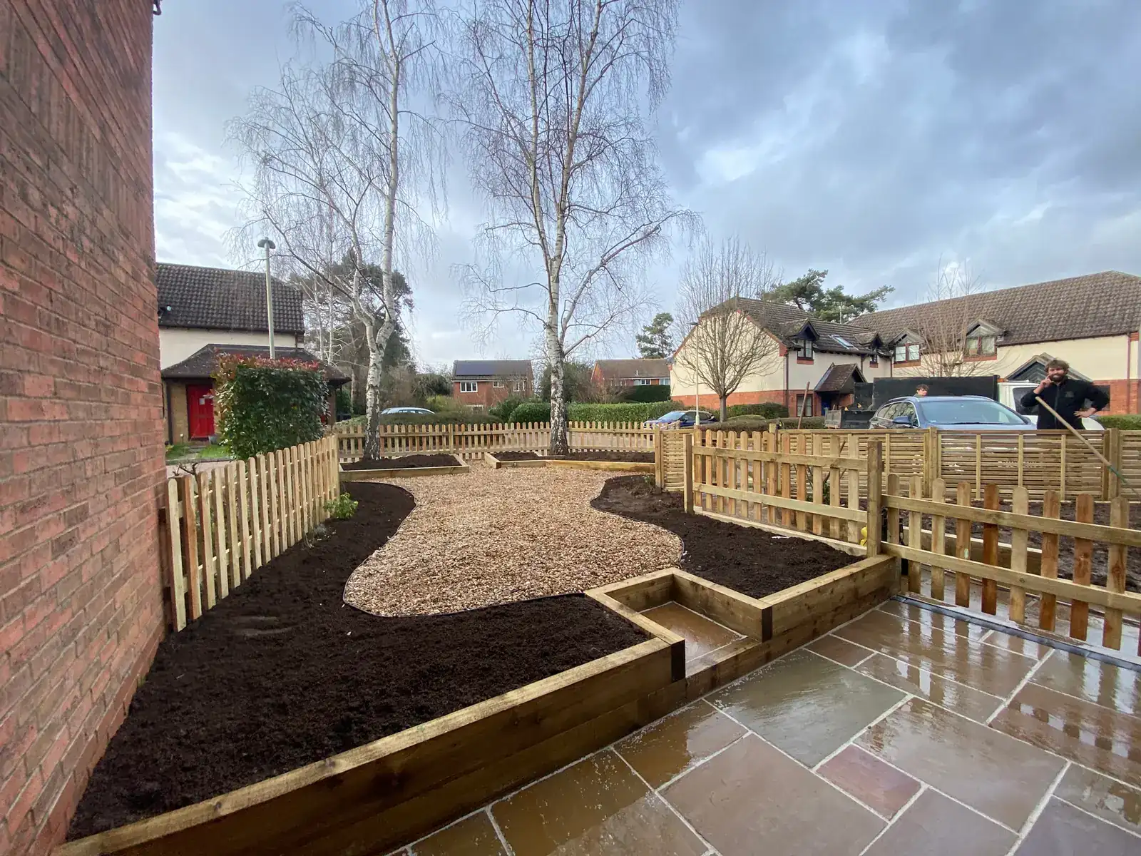After: the same garden in two level tiers, with a patio by the house, a step up to a shingle area, flower beds and a new picket fence