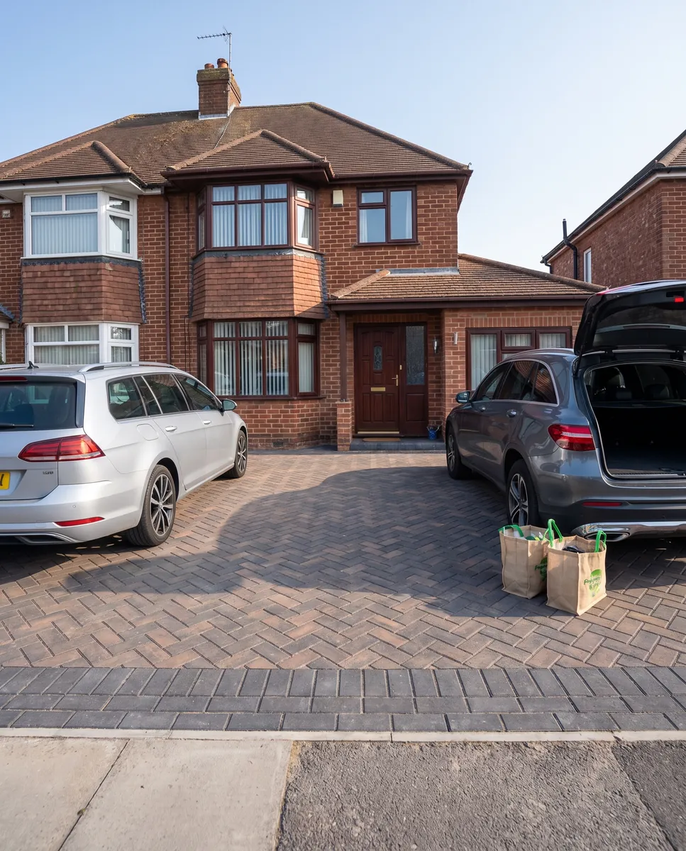 Illustration: two cars parked side by side on a wide, level block paving driveway, one boot open with shopping bags