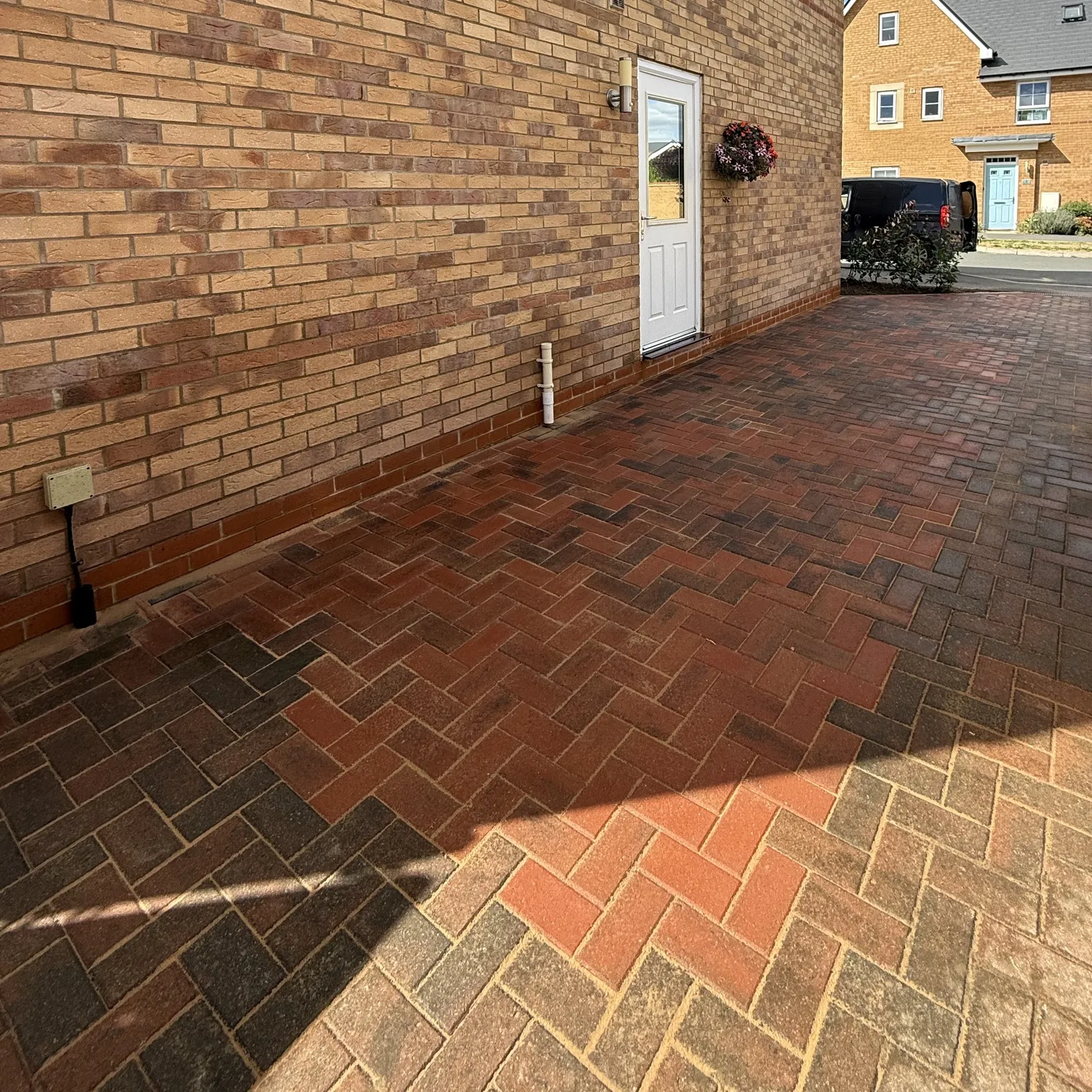 A block paving driveway extension in Milton Keynes: new red and brindle herringbone running alongside the house and into the existing drive
