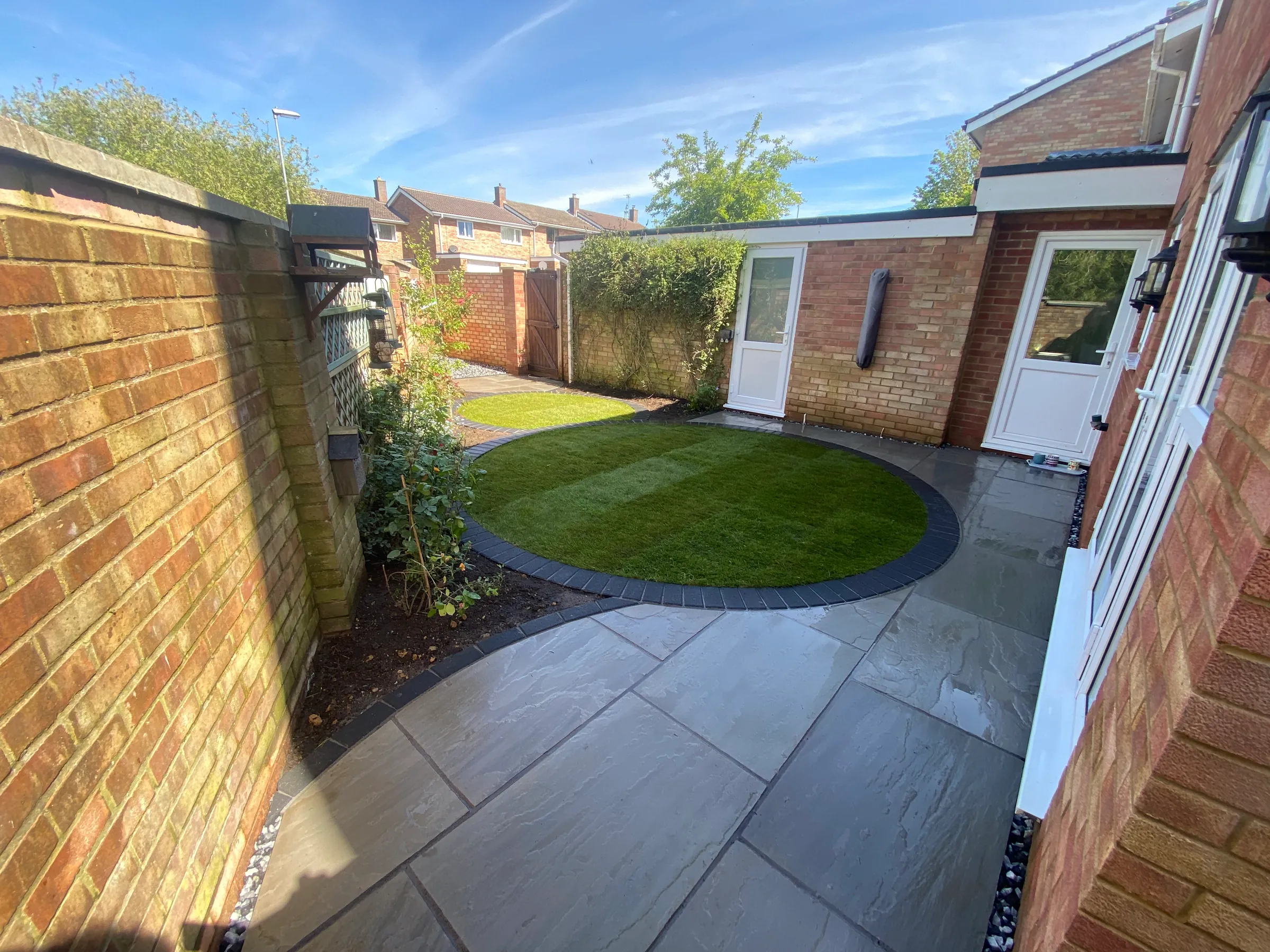 A finished garden in Langford: grey sandstone paving curving round a circular lawn beside the house